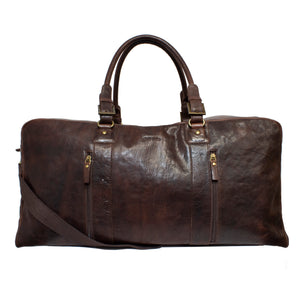 A large, dark brown Pierre Cardin Rustic Leather Overnight Bag with two sturdy handles, a detachable shoulder strap, and several zippered pockets on the front. This duffle bag has a spacious, rustic appearance with gold-tone hardware and a smooth, slightly weathered finish.