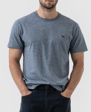 A man wearing the Rodd & Gunn The Gunn T-Shirt in heather blue, featuring a small red embroidered logo on the left chest. He has his hands in the pockets of his dark jeans. The casual tee is crafted from Australian Cotton, and the background is plain white.