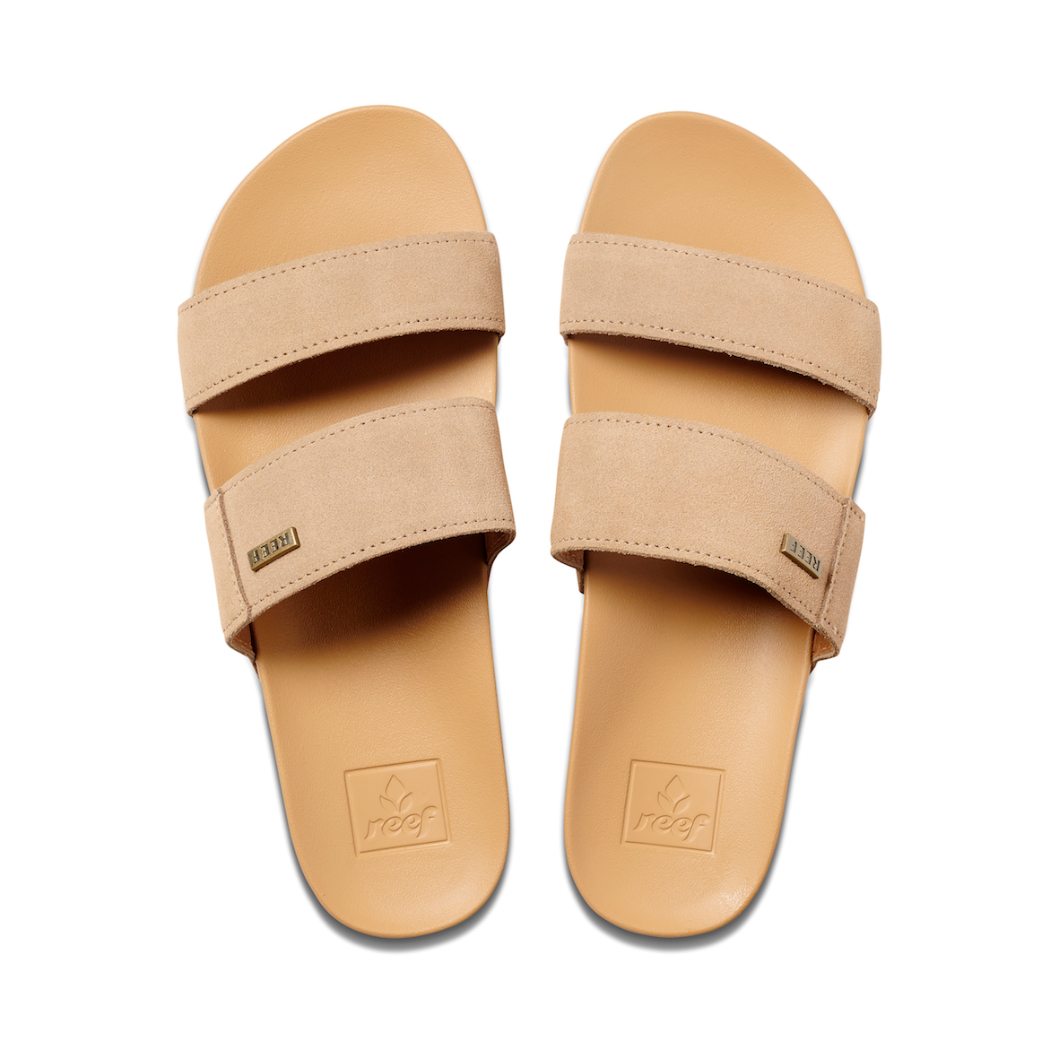 The REEF Cushion Vista Suede sandals, in tan, feature two wide vegan leather straps and a textured footbed. The "Reef" name appears subtly on tags and embossing. Their cushion bounce midsoles offer a blend of simple design and comfort, ideal for everyday wear.