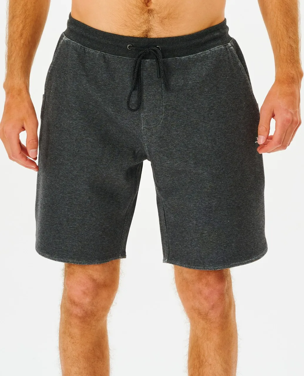 A person stands against a white background wearing Rip Curl Vaporcool Shorts in charcoal gray. The shorts feature a relaxed fit, large side pockets, and a subtle Vaporcool logo. Their hands rest casually at their sides.