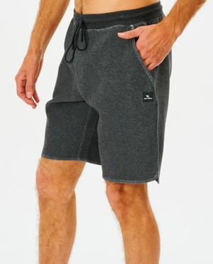 The person is wearing dark gray Rip Curl Vaporcool Shorts with a black drawstring and pockets, ideal for essentials. A small Vaporcool logo patch enhances the side. These comfortable shorts are stylishly displayed against a plain white background with their hand relaxed in the right pocket.