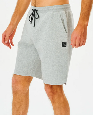 A person wears Rip Curl Vaporcool Shorts in light gray with a black drawstring and logo on the left leg. These comfy shorts have side pockets, perfect for lounging or workouts, shown against a white backdrop.