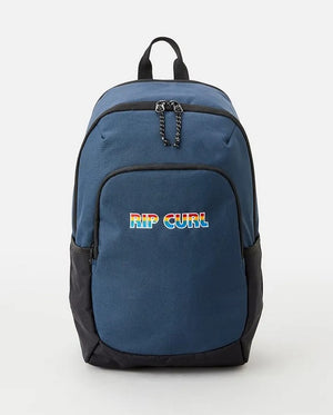 The Rip Curl Ozone 30L Icons Eco Backpack is a stylish blue backpack with black accents and a front pocket that proudly displays the logo in vibrant rainbow letters. Crafted from recycled plastic, this eco-friendly bag features two zippered compartments and durable black straps.