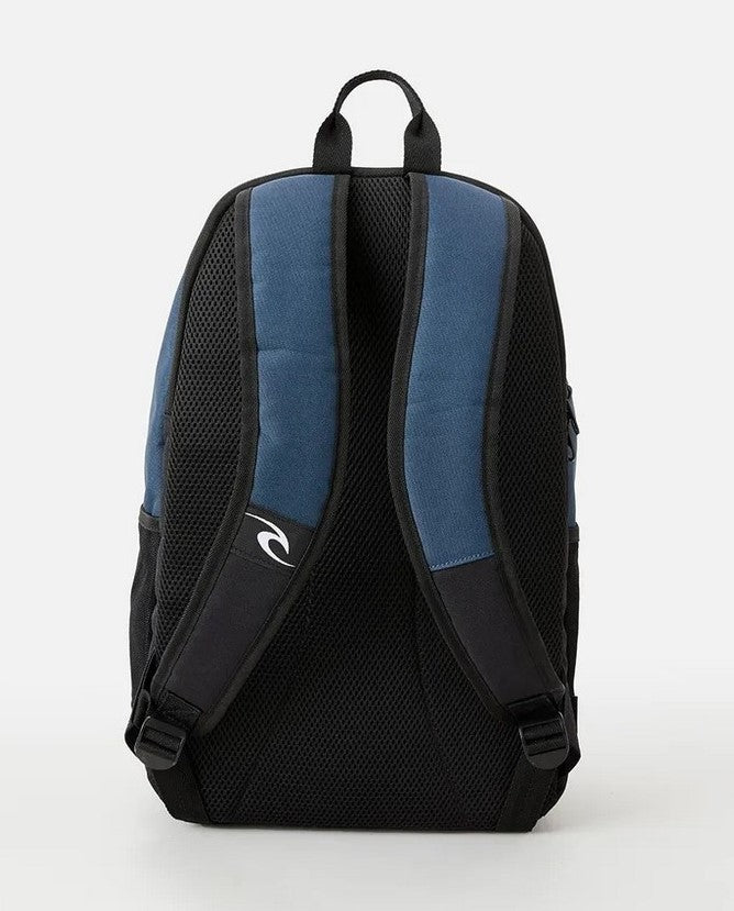 A Rip Curl Ozone 30L Icons Eco Backpack in blue and black is shown from the back. The backpack features two black padded shoulder straps with blue padding and a white logo on the right strap. Made from recycled plastic, it also includes mesh side pockets and a top handle for carrying.