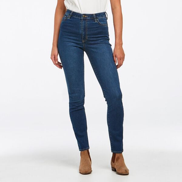 The person is dressed in Riders Classic High Slim Jean and a white top, gracefully posed against a plain white background. Tan ankle boots complement the slim-fit ensemble.