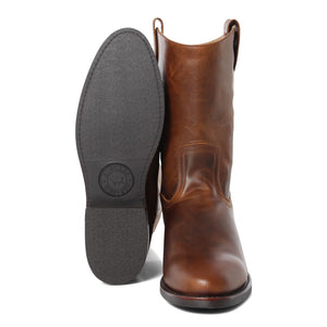 A pair of brown genuine leather cowboy boots are displayed. One Ringers Western Kimberley High Boot stands upright, showcasing its smooth, vintage finish, while the other is placed sole-forward, highlighting the brand's logo embossed on the heel's rubber sole.