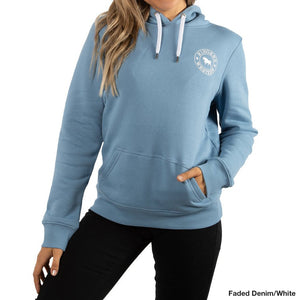 A person wearing a Ringers Western Women's Signature Bull Hoodie in faded denim, featuring a white emblem on the chest, stands with one hand in the front pocket. The casual and comfortable hoodie boasts white drawstrings and pairs perfectly with black pants. The background is plain white.