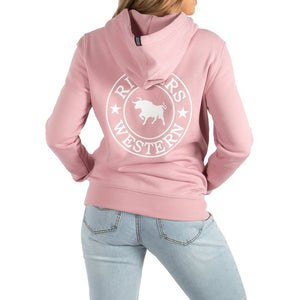 A person is wearing a Ringers Western Women's Signature Bull Hoodie in light pink with the hood up. The back of the hoodie features a large circular logo that includes the words "Ringers Western" and a silhouette of a bull in the center. They are also wearing light blue jeans.