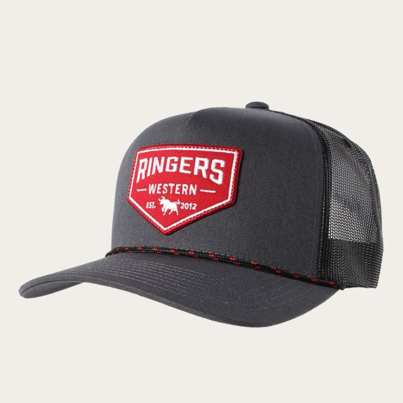 The Ringers Western Garage Trucker is a dark gray hat with a black mesh back and a curved brim. Its front panel showcases a red and white embroidered patch reading "Ringers Western" and "Est. 2012," accompanied by a small silhouette of either a cattle or cowboy figure. An adjustable strap guarantees the perfect fit.