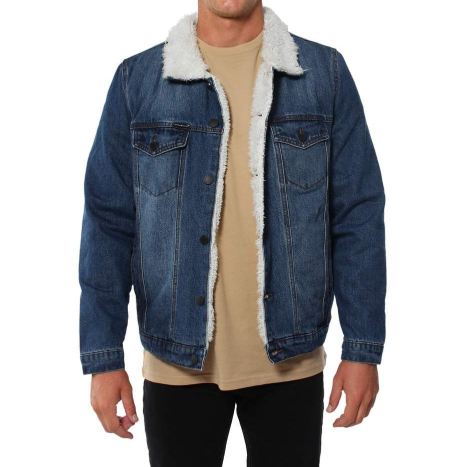 A man wearing a Ringers Western Duncan Denim Jacket with a white sherpa lining and collar, paired with a beige shirt and black pants. The jacket features button closures and chest pockets. The man's face is not visible.