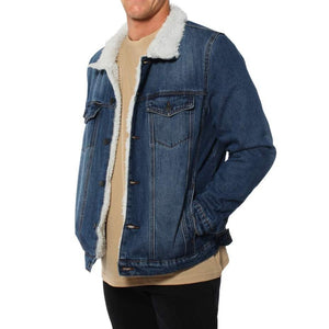 A person wearing a Ringers Western Duncan Denim Jacket with a cozy sherpa lining. The jacket is open to show a beige shirt underneath. The person stands with one hand in their pocket and the other at their side, against a plain white background.