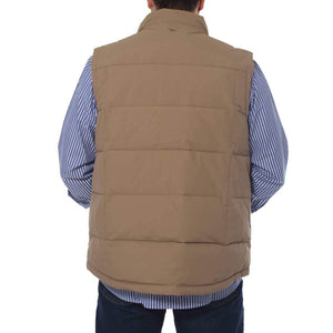 A person is seen from the back wearing a tan-colored Ringers Western Horsham Puffer Vest with a soft fleece lining over a blue and white striped shirt. The person has their hands in the pockets of the comfortable vest, and the bottom portion of dark blue jeans is visible. The background is plain and white.
