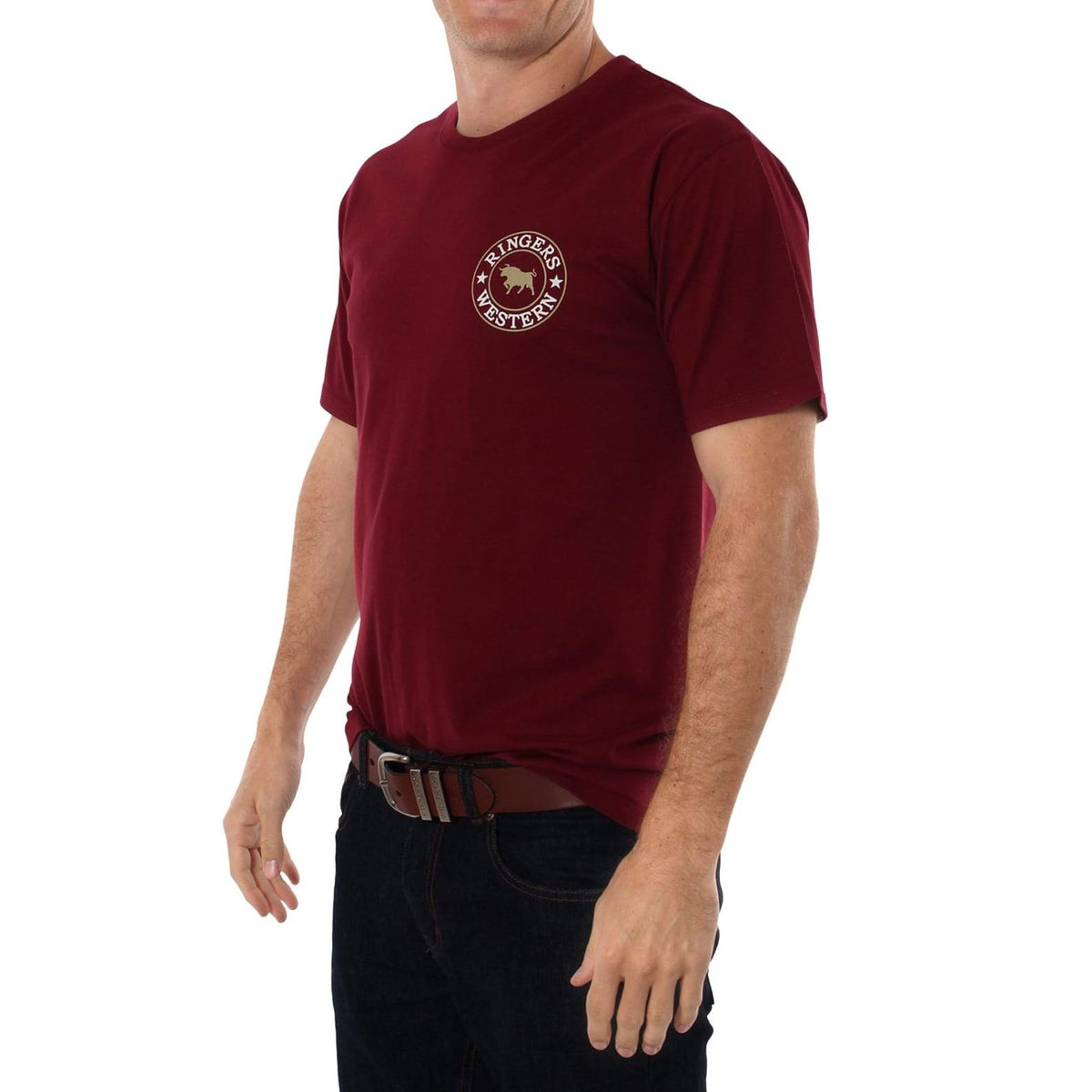 A person is wearing a Ringers Western Signature Bull Classic T-Shirt in maroon, featuring a crew neck and short sleeves, with a circular "Ringers Western" logo on the left chest. The comfortable T-shirt is paired with dark jeans and a brown belt, set against a plain white background. The person's face is not visible.