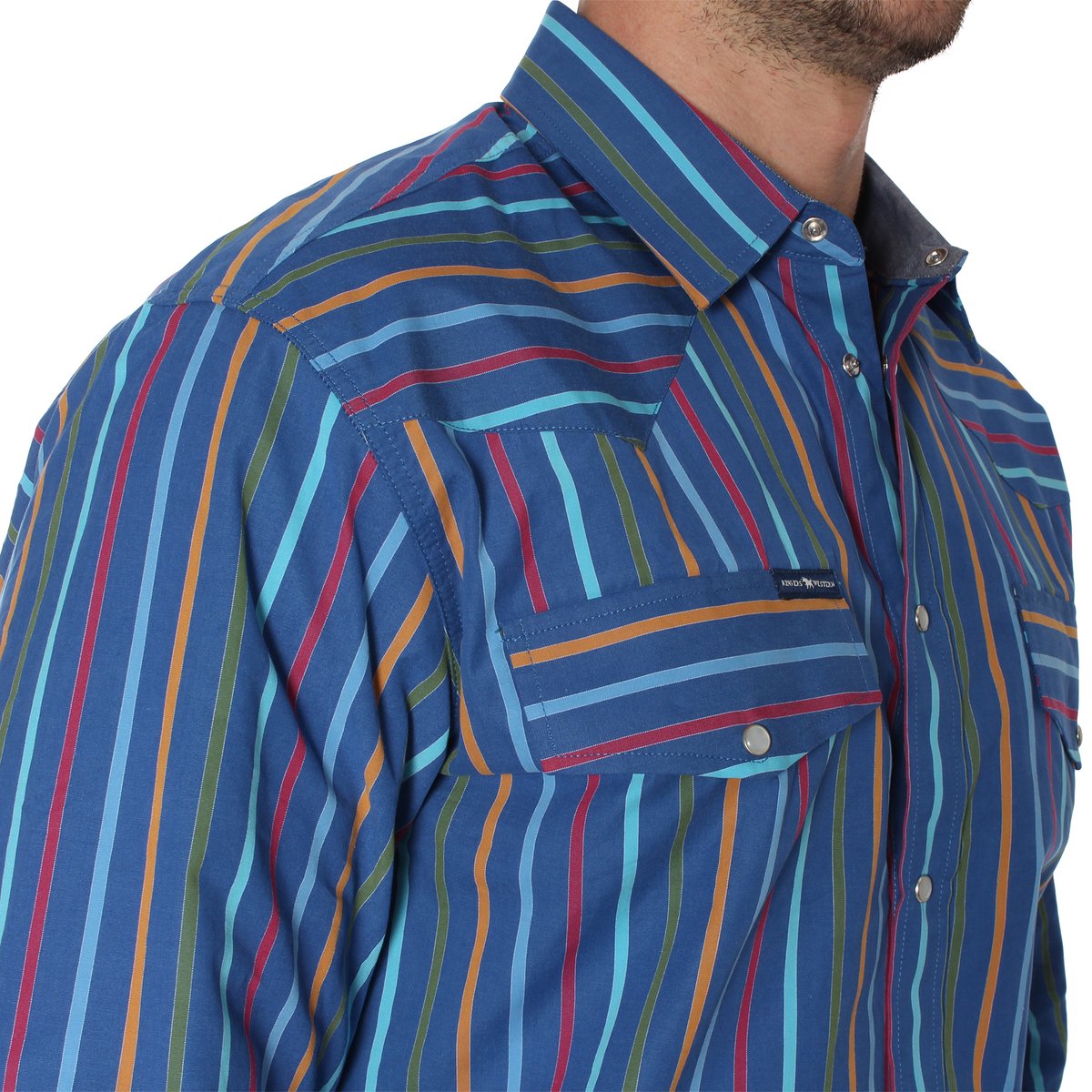 A person wearing the Ringers Western Wyoming Shirt, a semi-fitted blue button-up shirt with vertical stripes in various colors such as yellow, red, and shades of blue. The shirt is made of 100% cotton and features two front pockets with buttoned flaps and metal snaps. Only the upper torso of the person is visible.