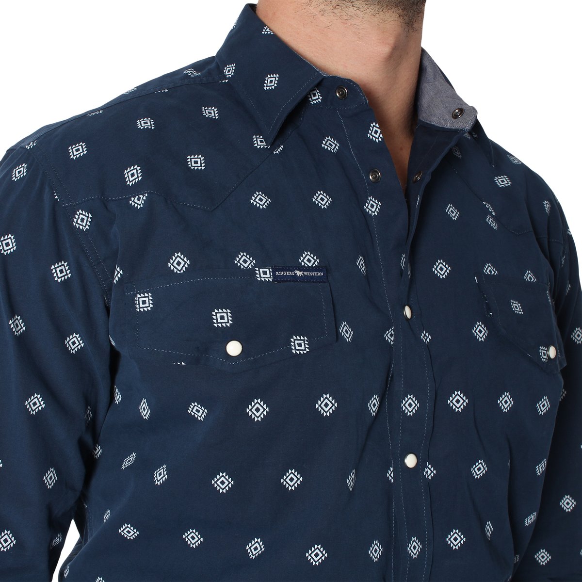 Close-up of a person wearing a dark blue, semi-fitted Ringers Western Wyoming Shirt with a white geometric diamond pattern. The 100% cotton shirt features a button-down front and two breast pockets. The person is pictured from the shoulders to the chest, set against a plain white background.