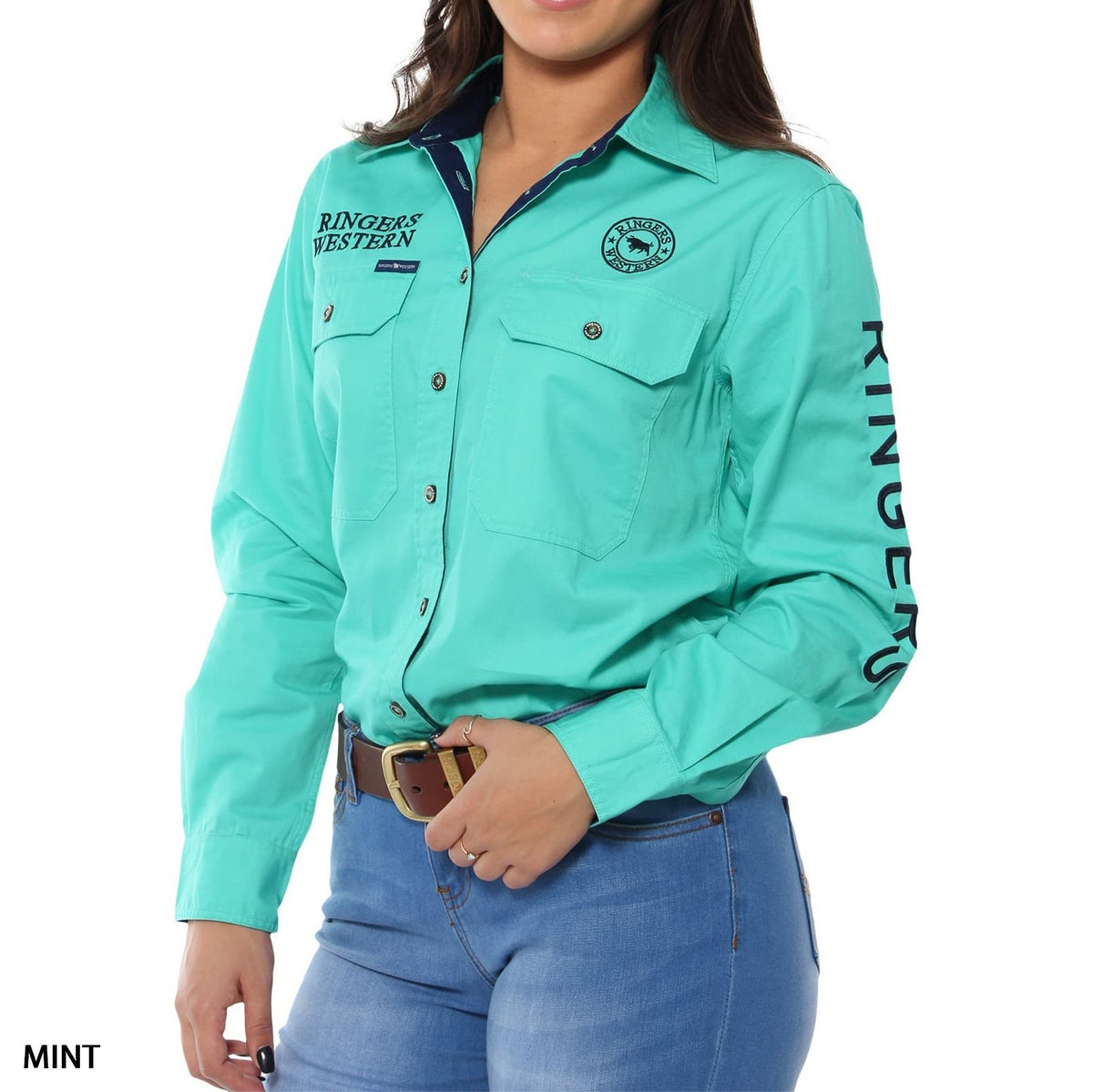 A woman wears a mint green Ringers Western Signature Jillaroo Womens Full Button Shirt (100% cotton, UPF50+, chest and sleeve logos), paired with light blue jeans and a brown belt; only her torso and lower face are visible.