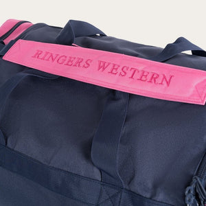 Close-up of a dark blue Ringers Western Rider Sports Bag featuring a pink handle with "RINGERS WESTERN" embroidered in capital letters. Several straps are visible around the bag, highlighting its design and durability, making it an ideal sports bag. The background is plain and neutral.