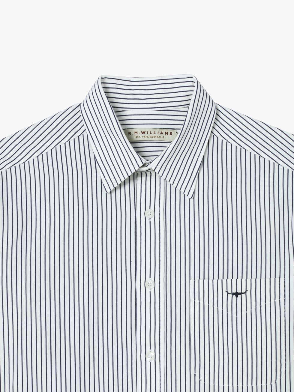 The RM Williams Collins Shirt, in white with thin black vertical stripes, is made from smooth twill cotton and includes a pointed collar, button front, front pocket, and visible brand label inside the collar.