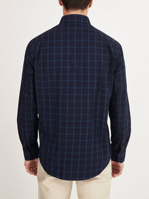A man is shown from the back wearing the RM Williams Collins Shirt, a navy blue, long-sleeved, 100% cotton button-up with a light blue checkered pattern, paired with light-colored pants.