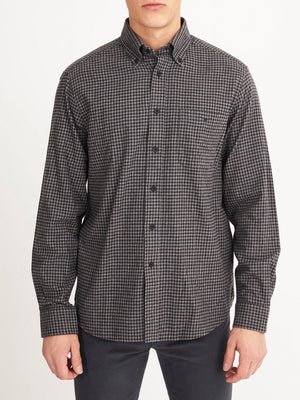 A person wears the RM Williams Collins Shirt, a long-sleeved, button-up shirt in black and gray small checkered brushed cotton, paired with dark pants and standing against a plain white background.