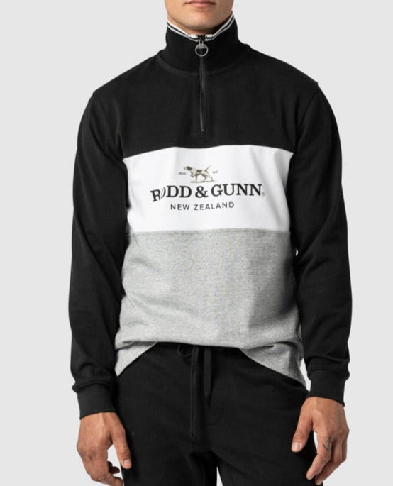 A person is wearing a Rodd & Gunn Hillop Sweat jumper in black, white, and grey 100% cotton, featuring a "Rodd & Gunn New Zealand" logo on the front. The stylish half-zip sweatshirt has a high collar, and they are standing with hands in pockets against a plain background.