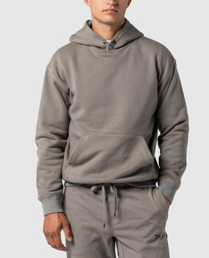 A person is wearing a light gray Rodd & Gunn Worser Bay Sweat hoodie paired with matching gray sweatpants. The hoodie, featuring ribbed cuffs and hem along with a front pocket, includes a soft fleece lining for extra coziness. The outfit appears relaxed and suitable for casual wear or lounging.