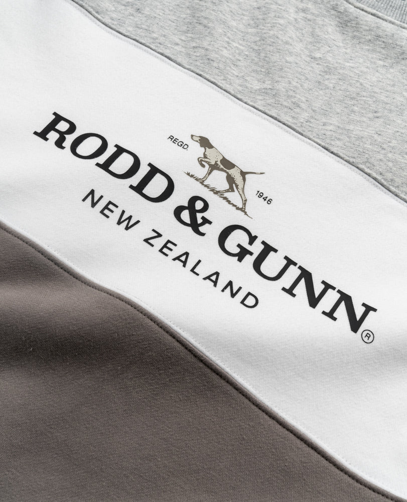 Close-up of a fabric panel from the Rodd & Gunn Mount Wesley Sweat, showcasing "Rodd & Gunn New Zealand" text and a dog logo. The fabric features light gray, white, and dark gray horizontal stripes with a cozy fleece lining for supreme comfort.