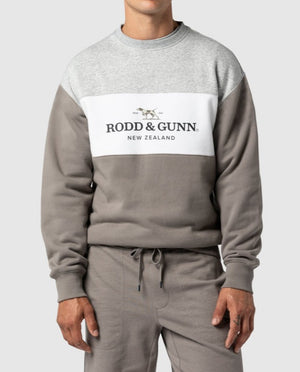 A man wears a Rodd & Gunn Mount Wesley Sweat in grey and white, displaying a running dog graphic and a color-block design. Its soft fleece lining complements his matching grey sweatpants perfectly.