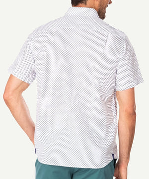 The image shows a man from the back, wearing a short-sleeved, white Gazman Linen Blend Pineapple Print shirt made of breathable fabric with a small black dot pattern. The comfortable shirt has a regular fit. He is also wearing teal pants. His right hand is partially visible, resting near his hip.