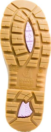 The image displays the underside of a light brown boot sole with a rugged tread pattern, characteristic of Steel Blue Southern Cross Ladies Zip Scuff Boots. The construction boot's sole features multiple deep grooves and a distinctive paw print design, accompanied by text and branding engraved near the center.