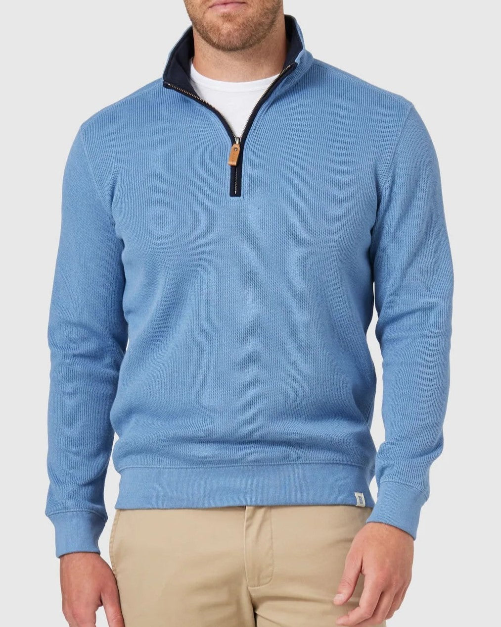Wearing a light blue Blazer Heather Half Zip Sweat with a black collar and tan zipper pull, paired with beige pants creates casual sophistication. The plain, light-colored background enhances the ensemble's relaxed vibe effortlessly.