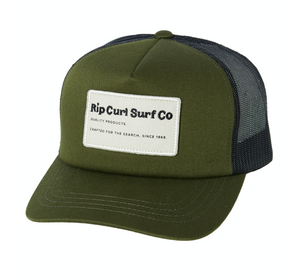 The Rip Curl SWC Trucker Hat in olive green features a black mesh back and an adjustable strap. It sports a rectangular white patch on the front panel with the text, "Rip Curl Surf Co, Quality Products, Crafted for the Search, Since 1969" in black. Made from durable cotton twill for lasting wear.
