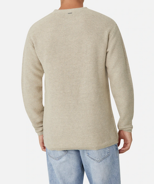 A person is seen from the back, wearing the Industrie The Washed Culver Knit, a stylish and textured light beige 100% cotton sweater with ribbed cuffs and a relaxed fit, paired with light blue jeans. The background is plain white.