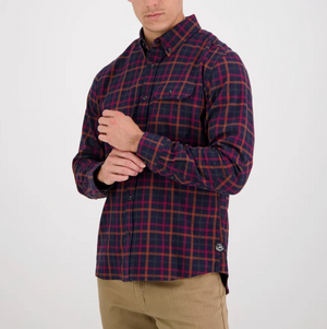 Dressed in a classic fit red and blue plaid Swanndri Fernald Point Shirt, made of 100% cotton, with khaki pants, the person stands against a plain white background, one arm crossed while adjusting the shirt sleeve with the other hand.