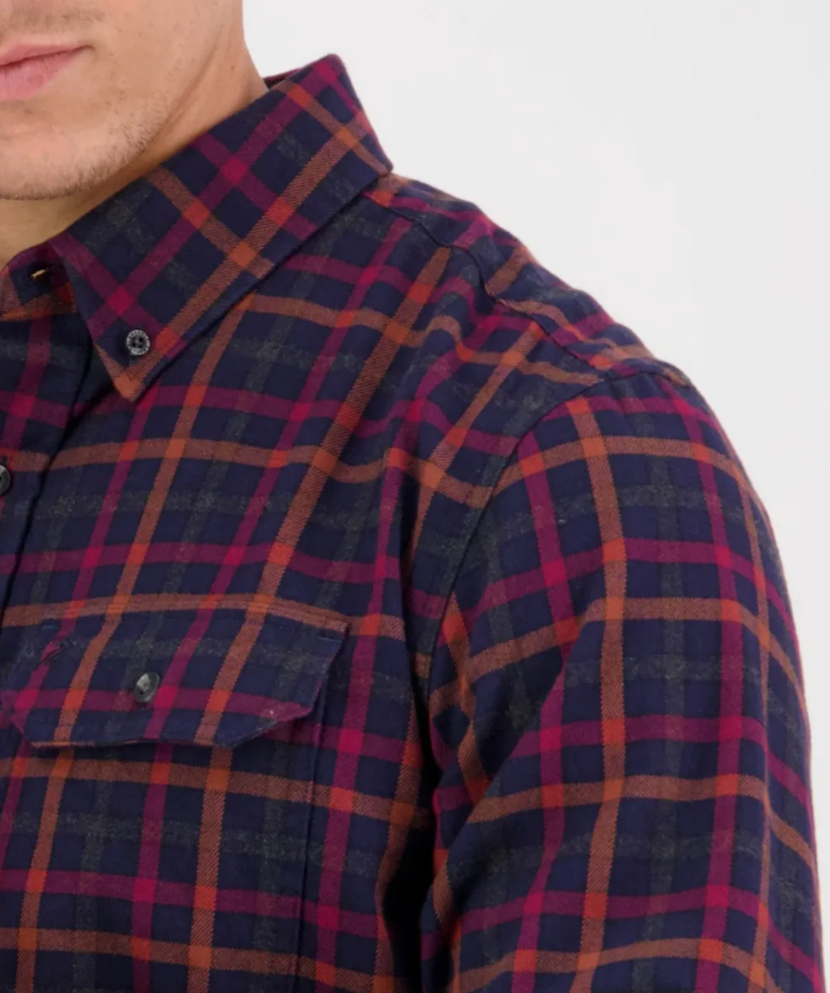 Close-up of a person wearing a Swanndri Fernald Point Shirt in classic fit, highlighting the intricate blue and red plaid design. The focus is on the 100% cotton texture, with part of the person's face and shoulder subtly visible.