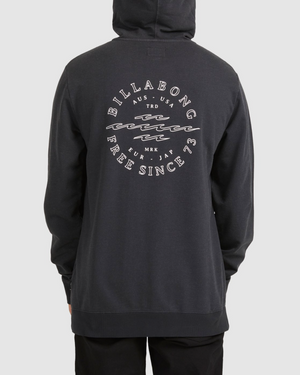A person seen from the back in a black Billabong Big Wave Dan Hood, featuring a circular white graphic with wavy lines and the text "Billabong Free Since '73" plus country abbreviations.