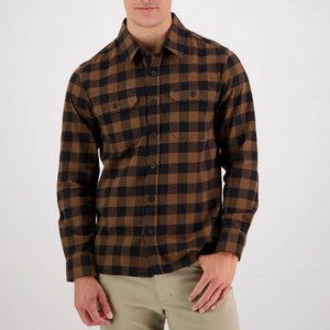A person wearing the comfortable 100% cotton Swanndri Taranaki Tailor Shirt in a brown and black checkered flannel pattern and khaki pants stands in front of a plain, light-colored background. The shirt features long sleeves and buttoned front pockets. The person is casually posing with one hand in their pants pocket.