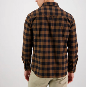 A person stands facing away from the camera, wearing a long-sleeved, 100% cotton Swanndri Taranaki Tailor Shirt in a brown and black checkered pattern, paired with light beige pants. The background is plain white.