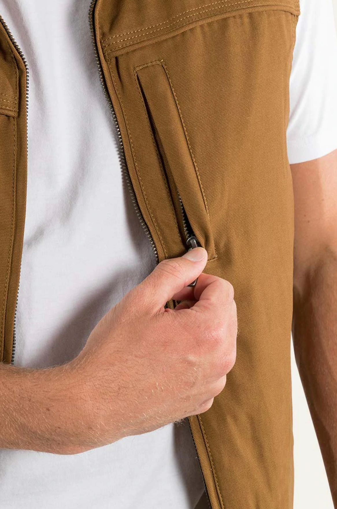 Someone in a white shirt is zipping up the Ringers Western Macquarie Canvas Vest, with a focus on their hand gripping the zipper of this cozy, sherpa-lined layer.