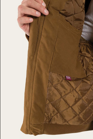Someone holds open the brown quilted Ringers Western Kalgoorlie Long Canvas Jacket, showing its inner lining and a small red tag. The jacket, featuring diamond-pattern stitching, appears to be held by the person's left hand.