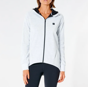 A person in a Rip Curl Anti Series Flux II Zip hoodie, light gray with a black hood lining and small chest logo, paired with black leggings against a white background, is showcasing ideal winter attire renowned for its durable water-resistant features.