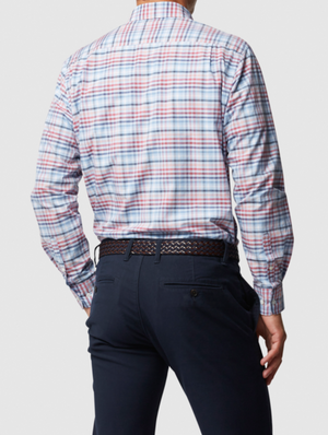 A man wearing the Rodd & Gunn Great Exhibition Bay Sports Fit Shirt, a stylish long-sleeved plaid crafted from 100% cotton in vibrant blue and red, stands with his left hand in his pocket. The sports fit complements his dark pants against a plain background.