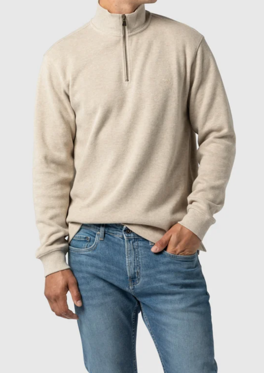 A person is wearing a Rodd & Gunn Alton Ave Sweat in light beige, made from 100% cotton, paired with blue jeans. They have one hand in their pocket against a plain white background.