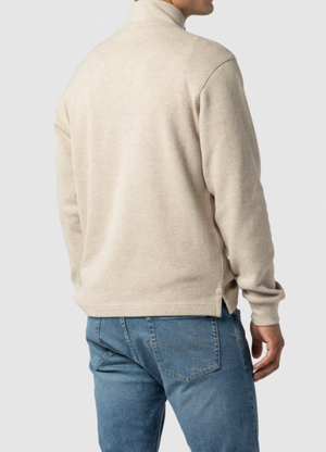 A person standing with their back to the camera, wearing a beige long-sleeve Rodd & Gunn Alton Ave Sweat and blue jeans. The background is plain and light-colored.