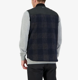 A person is seen from behind wearing the Swanndri West Melton Wool Vest, featuring a dark plaid pattern and quilted lining, over a grey sweatshirt. They stand against a plain white background, complemented by dark pants.