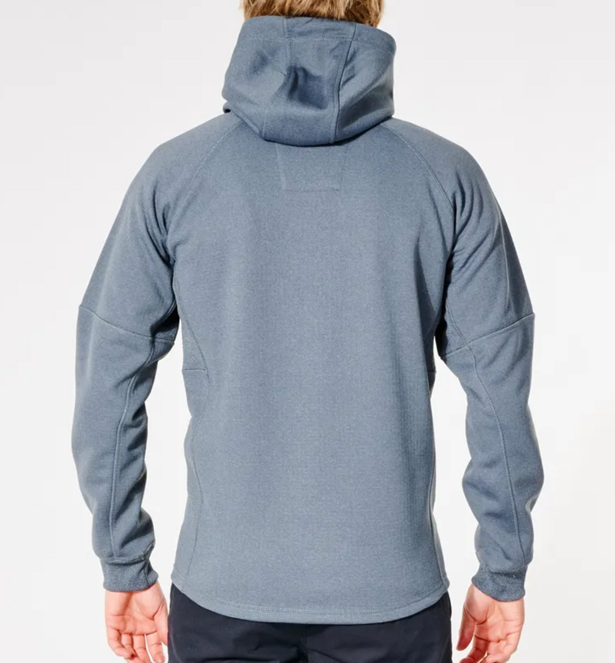 The individual is wearing the Rip Curl Anti Series Storm Zip Thru in blue-gray, featuring long sleeves and a smooth finish with subtle seams, ideal for winter. Dark pants complement this outfit against a plain white background.