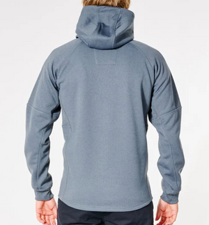 The individual is wearing the Rip Curl Anti Series Storm Zip Thru in blue-gray, featuring long sleeves and a smooth finish with subtle seams, ideal for winter. Dark pants complement this outfit against a plain white background.