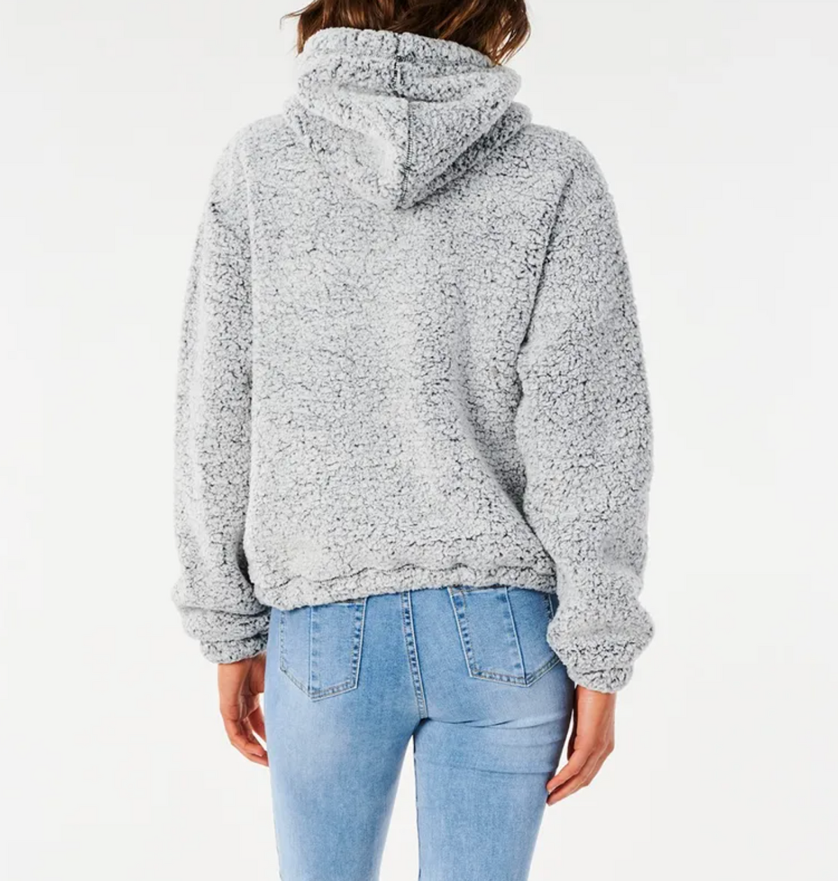 A person stands facing away from the camera, wearing a textured sherpa hoodie in light gray and light blue jeans. The Rip Curl Dark N Stormy Zip Thru hoodie covers their hair and has a slightly oversized fit with long sleeves. The background is plain white.