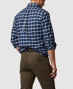 A person is seen from behind wearing a Rodd & Gunn Gunn Check Oxford Sports Fit Shirt in blue and white checks, crafted from 100% cotton, paired with olive green pants and a black belt. Their right hand rests on their hip, and their head is slightly turned to the right against a plain white background.