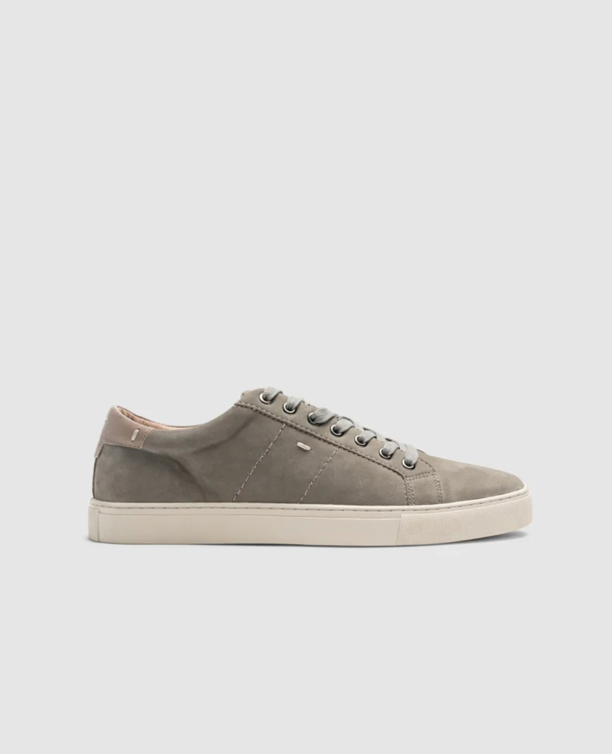 A side view of a single Rodd & Gunn Endeavour Spirit Sneaker in gray suede, featuring dark gray laces and a light beige rubber sole. This comfortable sneaker showcases subtle stitching details and a small tag near the laces, enhanced by nubuck leather accents that contribute to its simple, clean design. The background is plain and light gray.